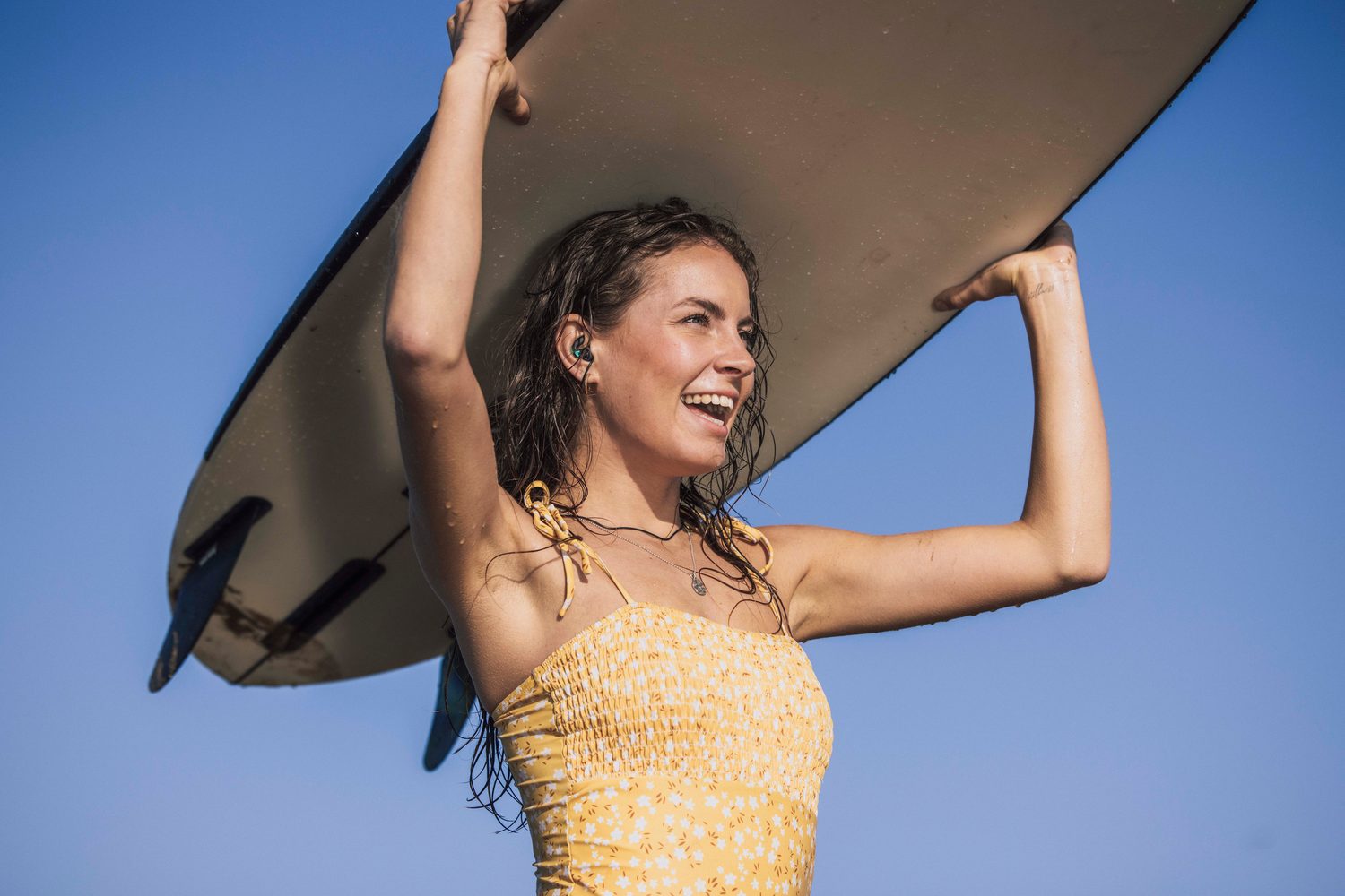 Woman smiling under a surfboard against a blue sky