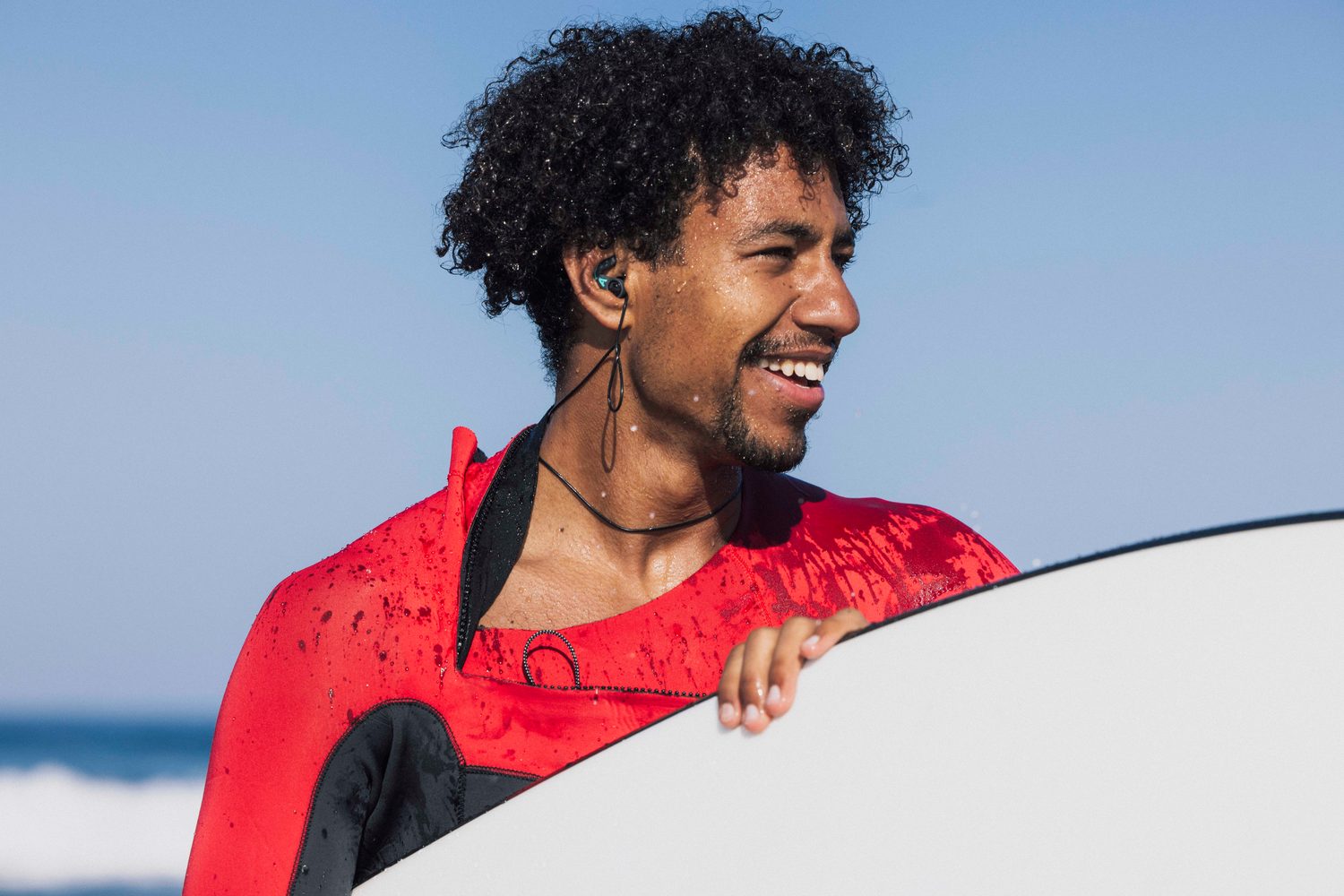 Surfer in a red wetsuit smiling with his board on the beach