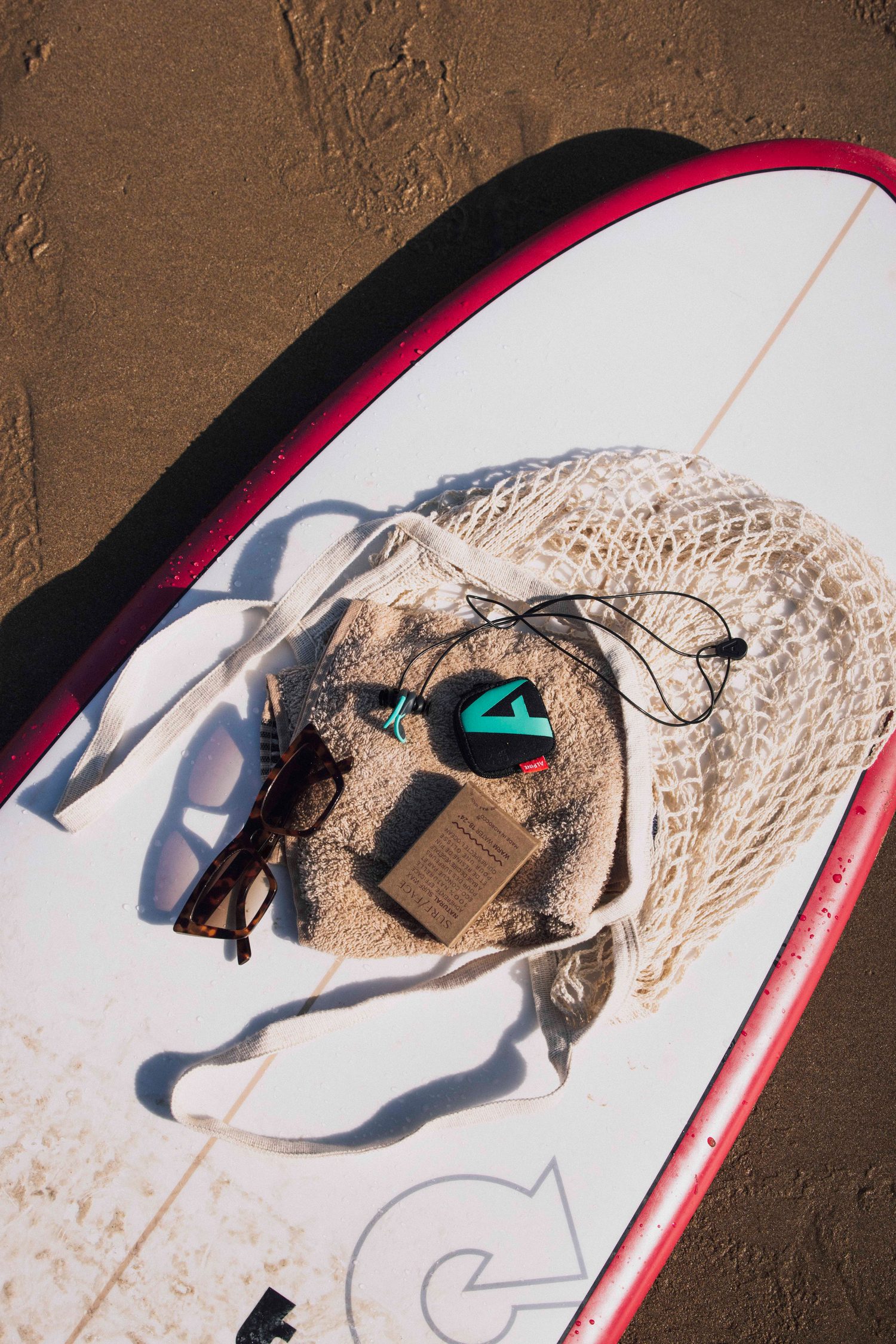Top view of a surfboard with a net bag, earplug case and sunglasses