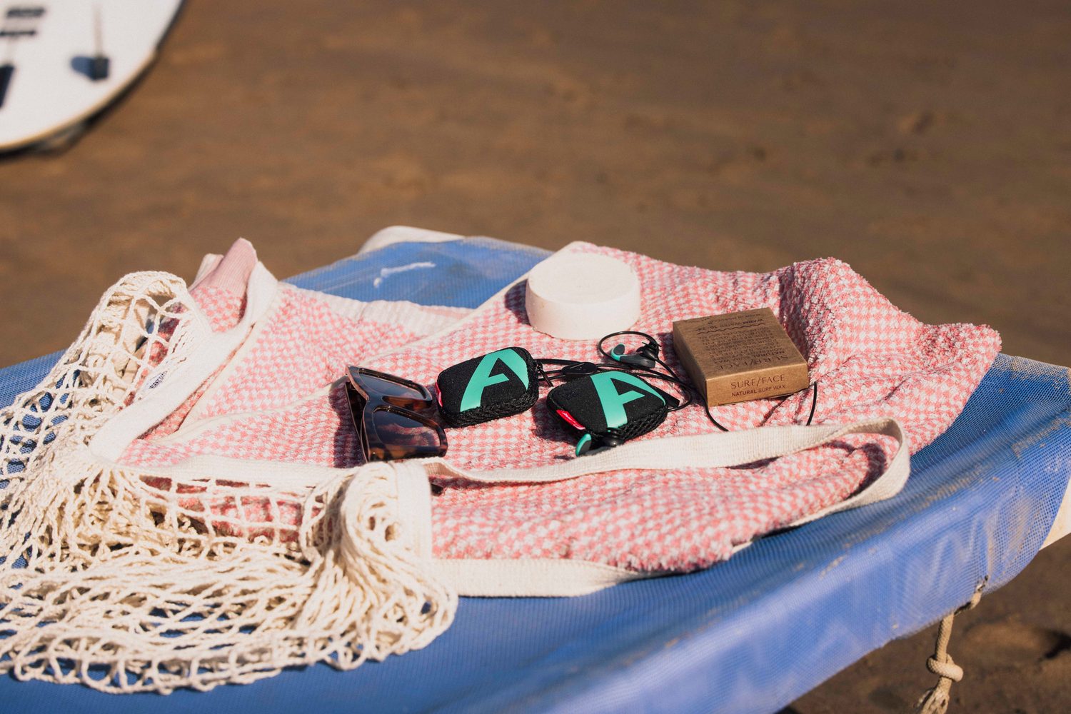 Beach towel with Alpine earplug cases, sunglasses and soap on a surfboard