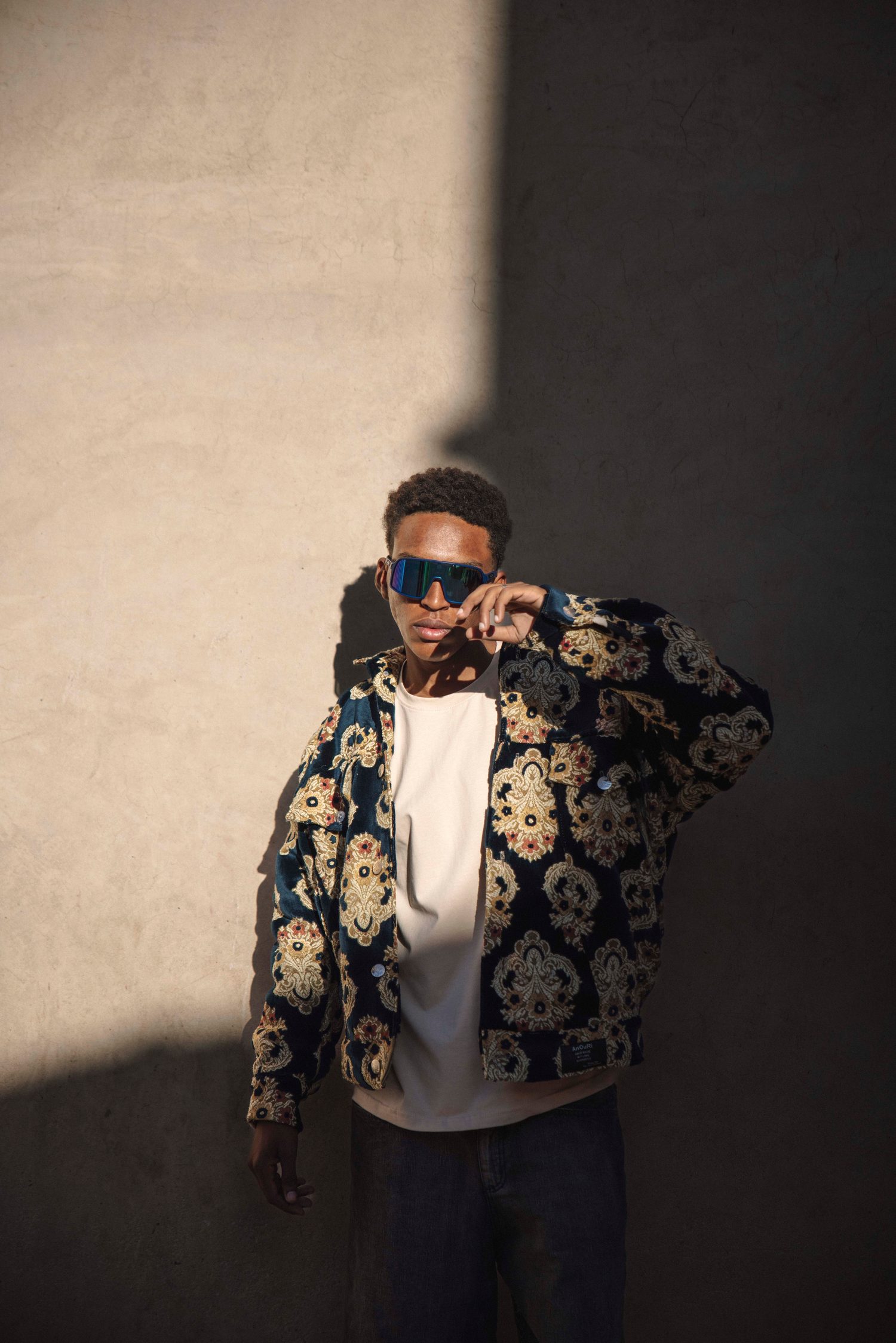 Model in sunglasses and a floral jacket against a wall with a hard shadow