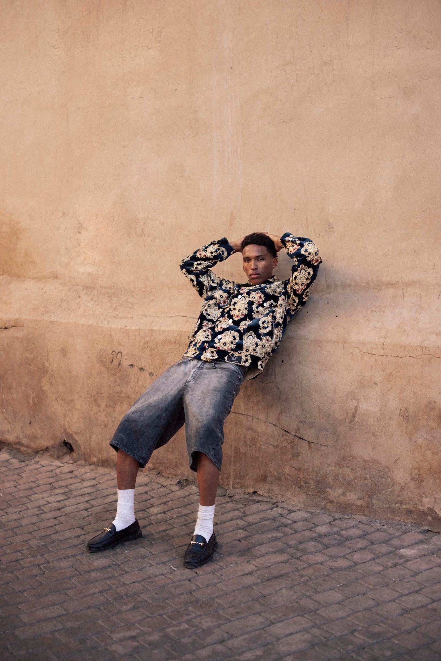 Model leaning back against a wall, arms behind his head