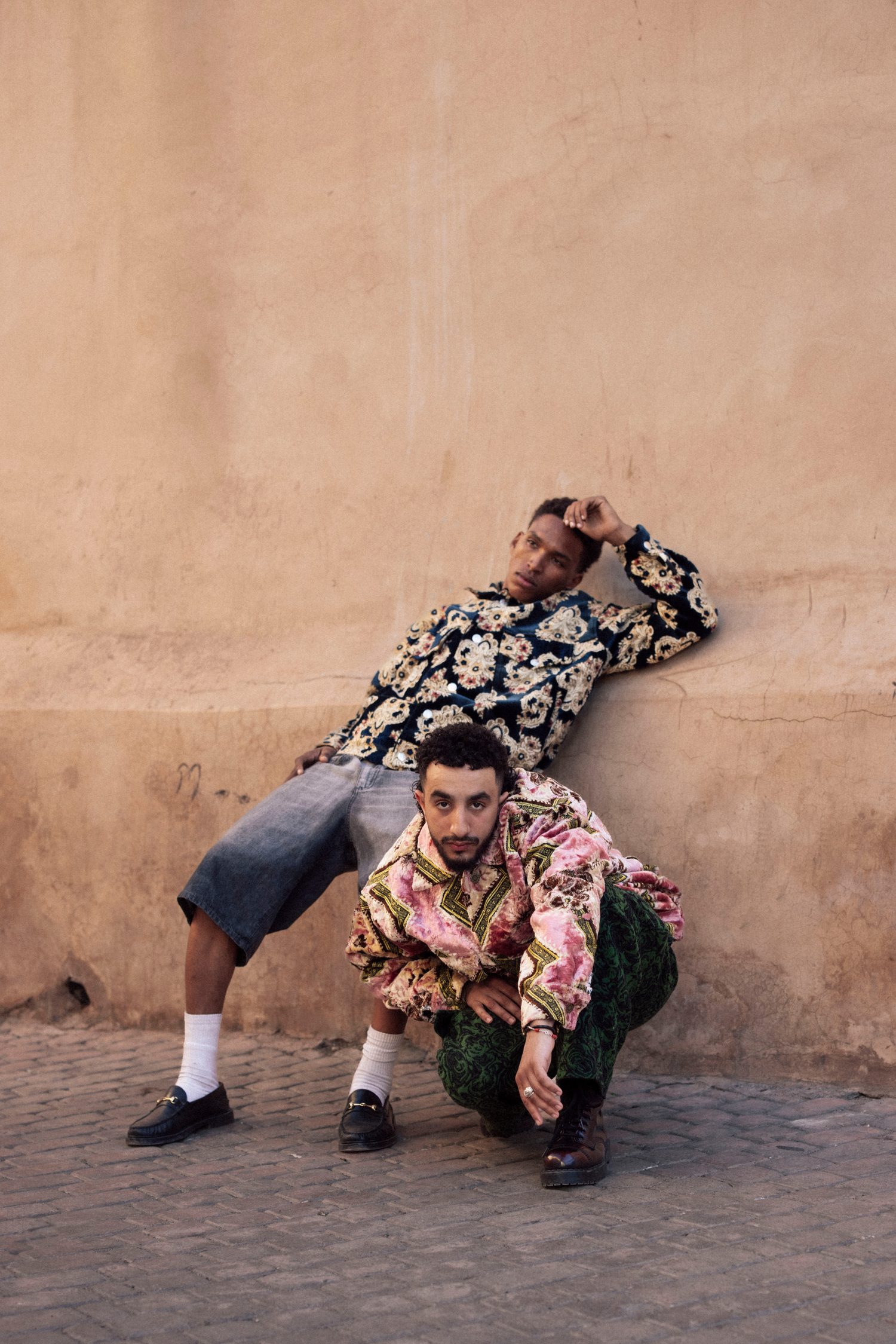 Two models posing against a wall, one standing and one crouching