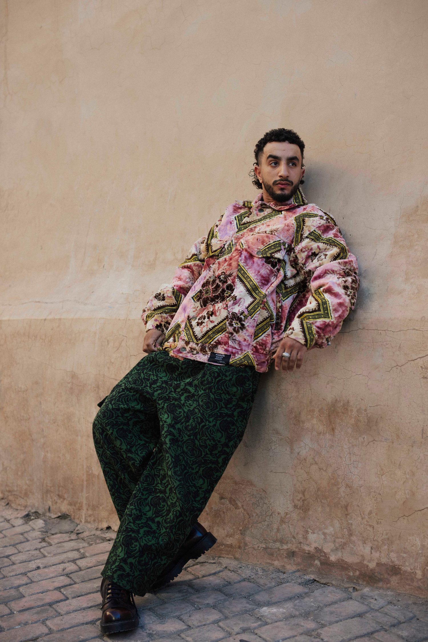 Model in a pink brocade jacket leaning against an ochre wall