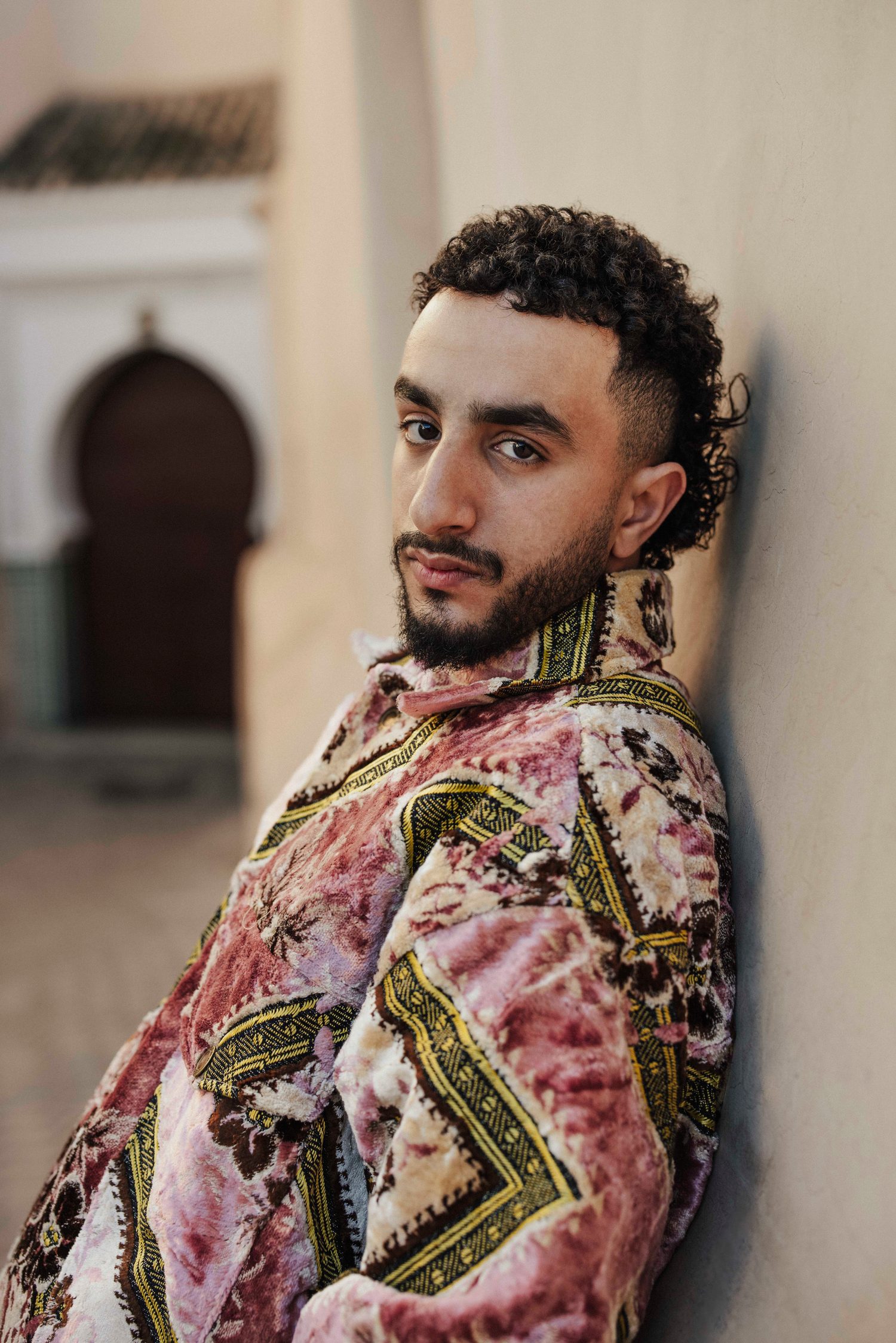 Close-up of a model in a pink brocade jacket leaning against a wall