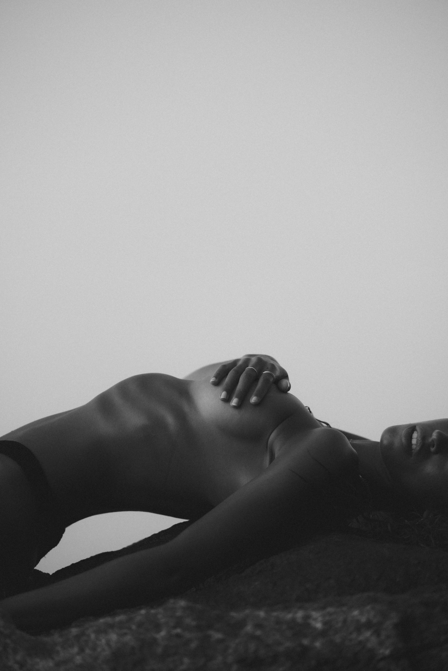 Woman reclining on a rock against a pale sky, in black and white