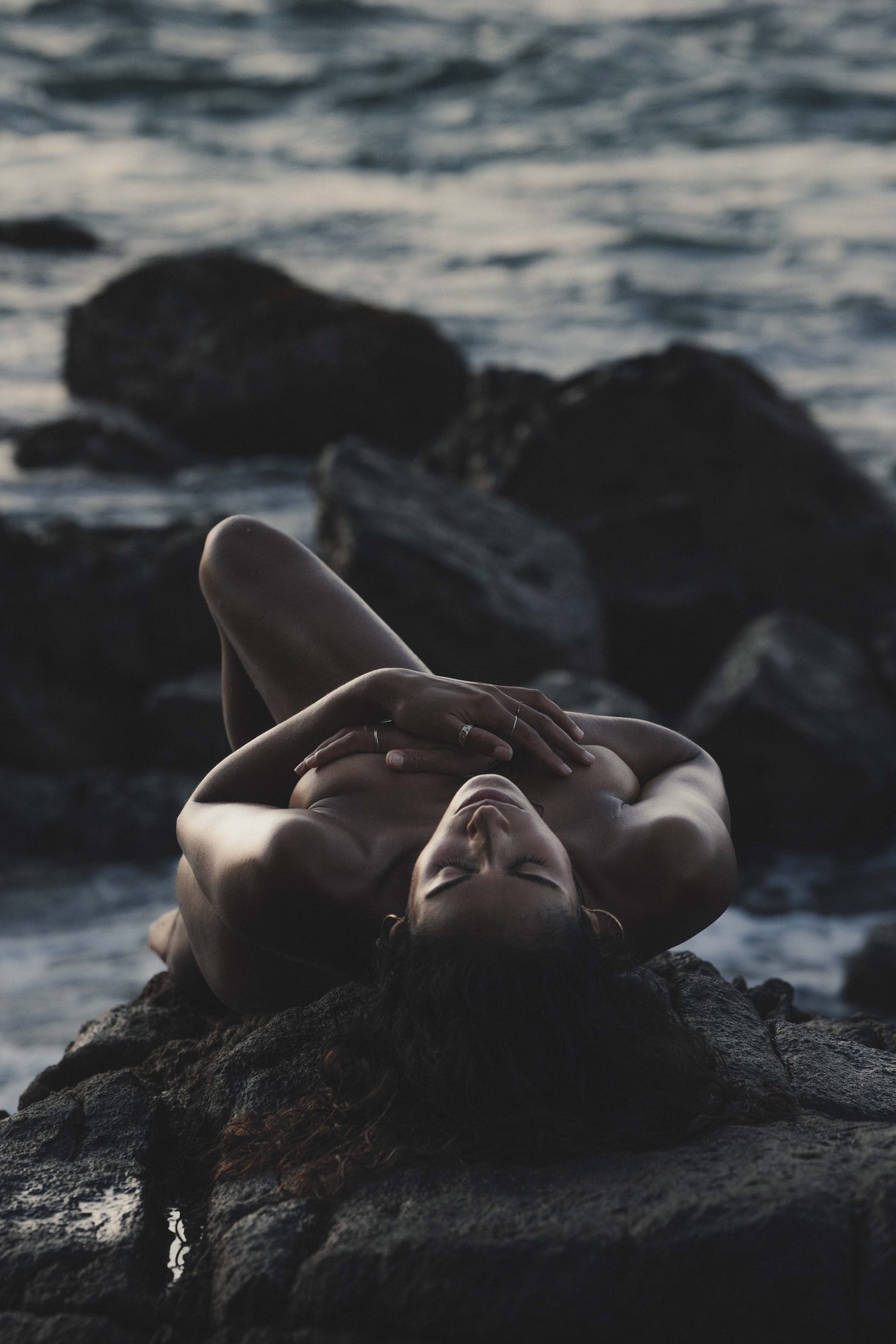Woman lying on dark rocks by the sea