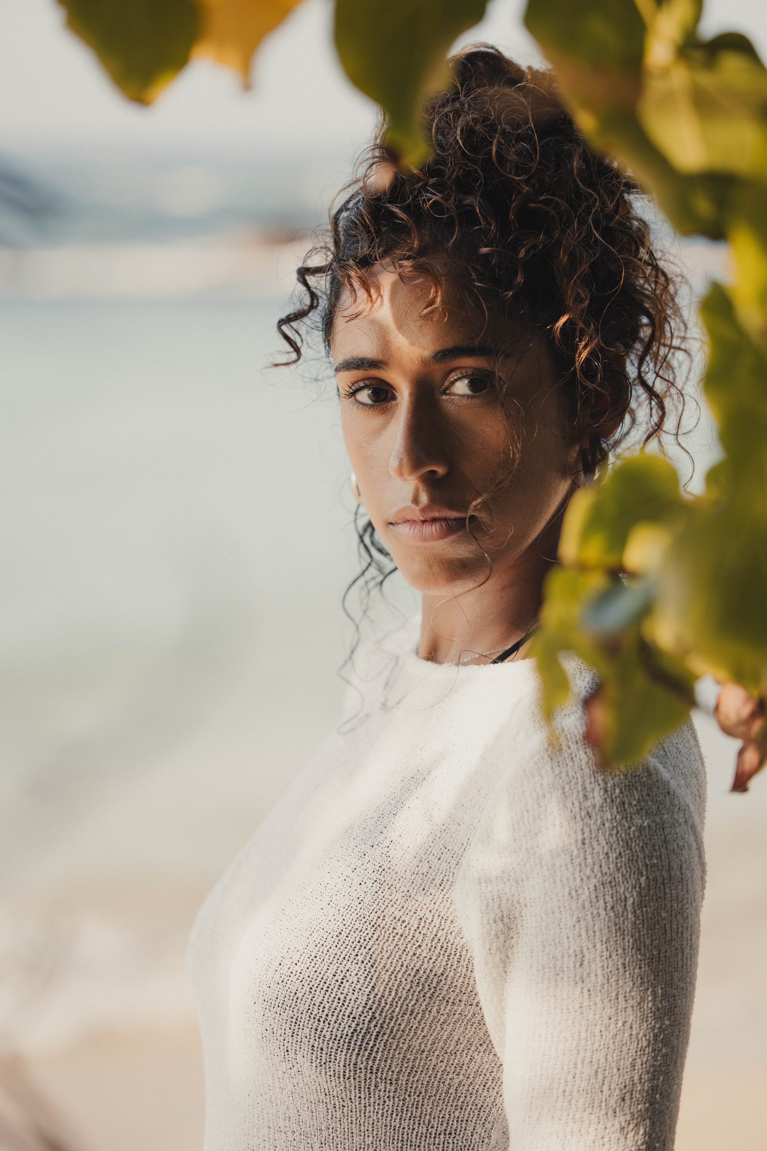 Portrait of a woman with curly hair in a white knit, framed by leaves