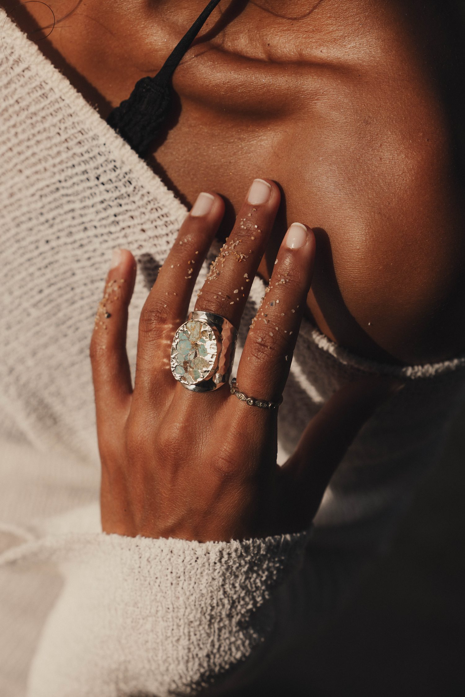 Hand with a large statement ring against a white knit