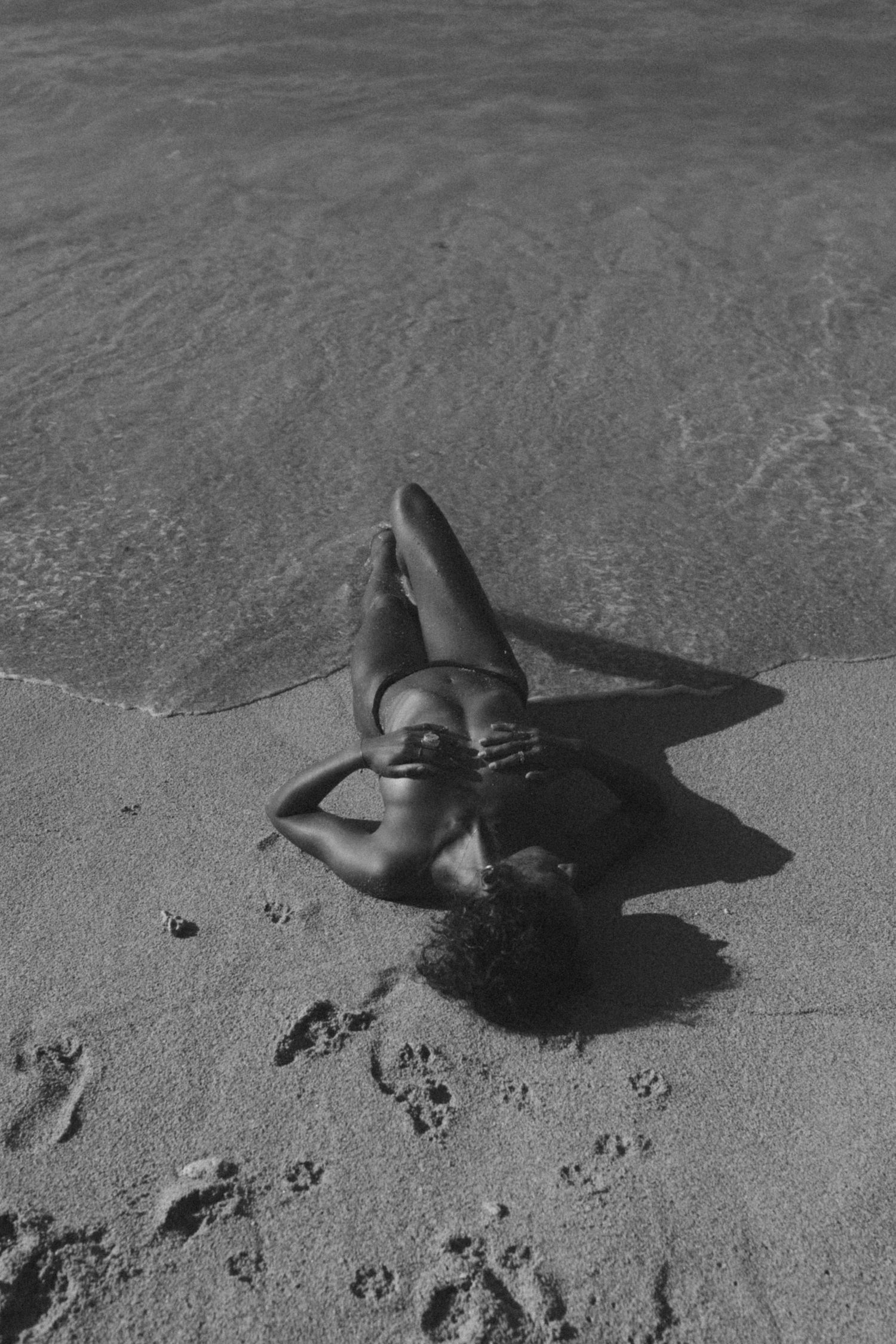 Woman lying in the sand at the water line, seen from above