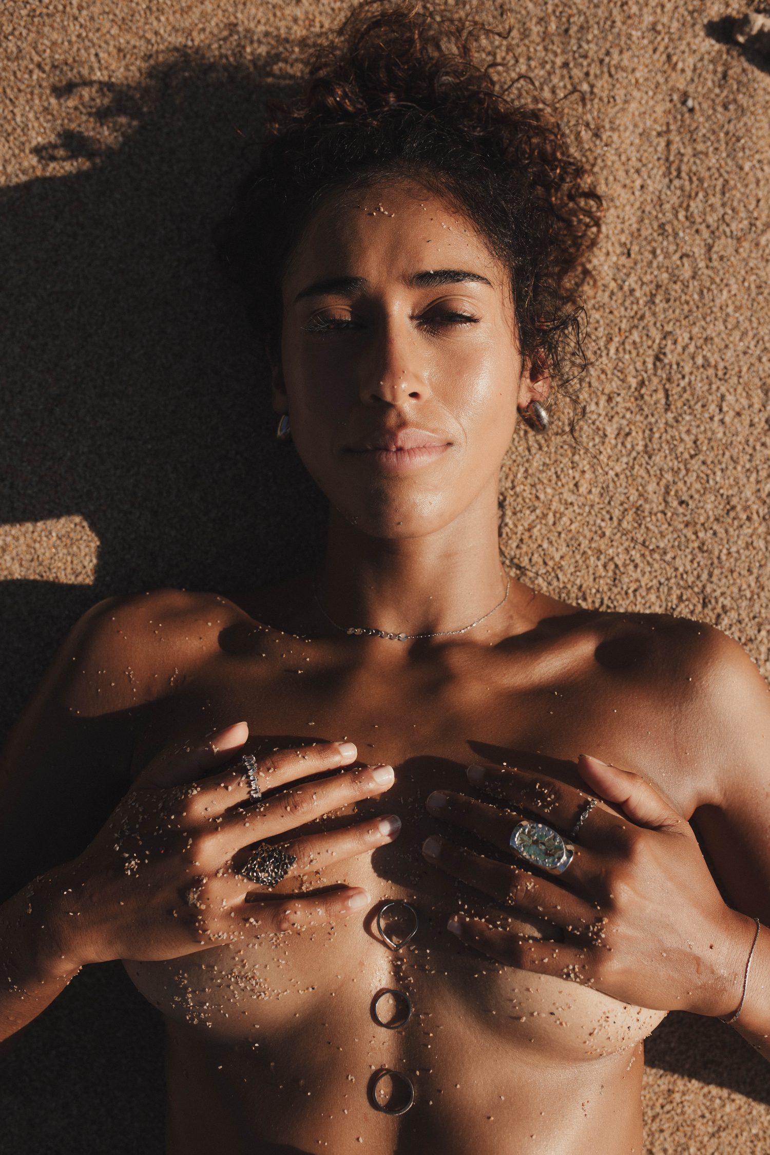 Woman lying in the sand wearing rings and a necklace