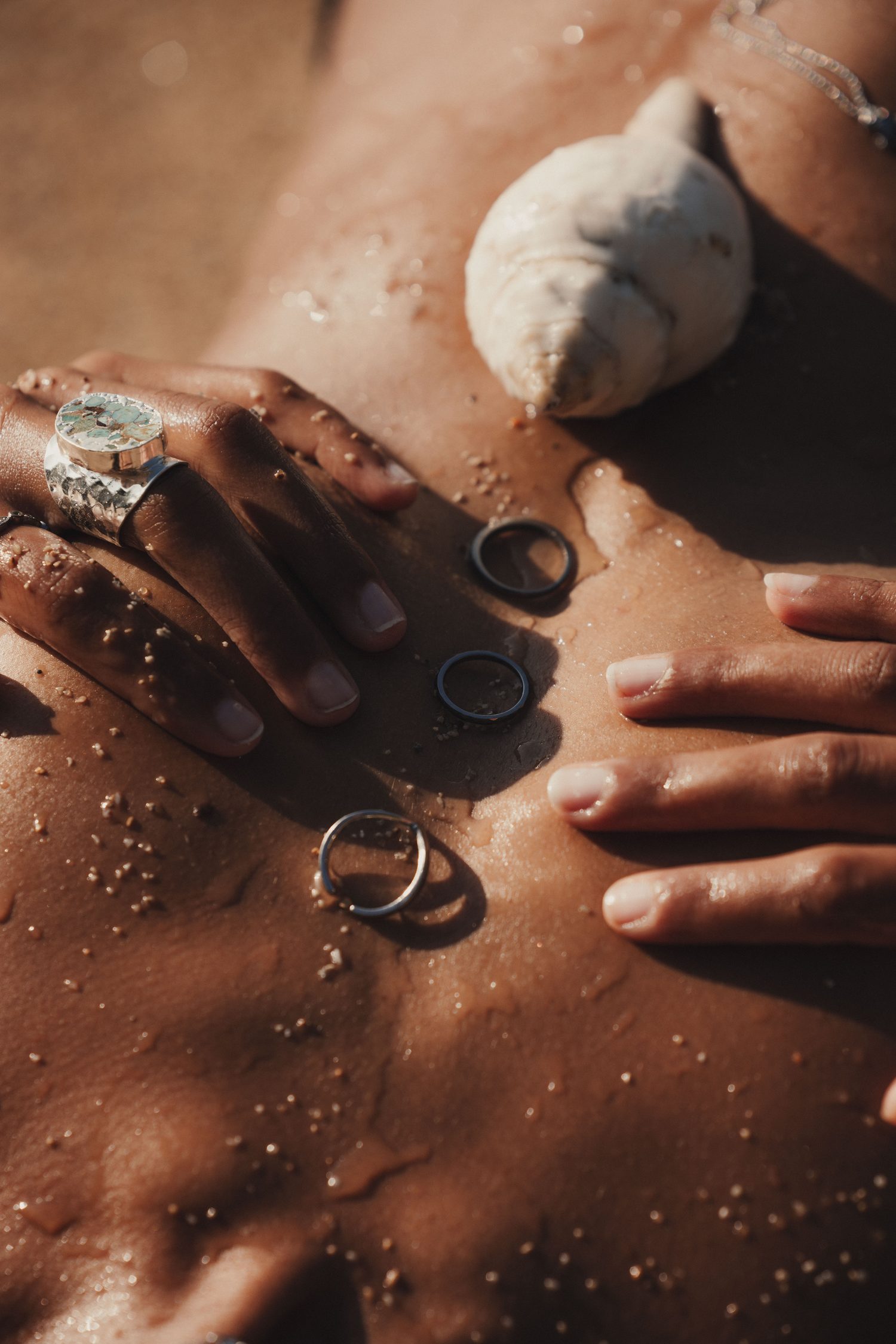 Rings and a shell on skin covered in sand, close-up