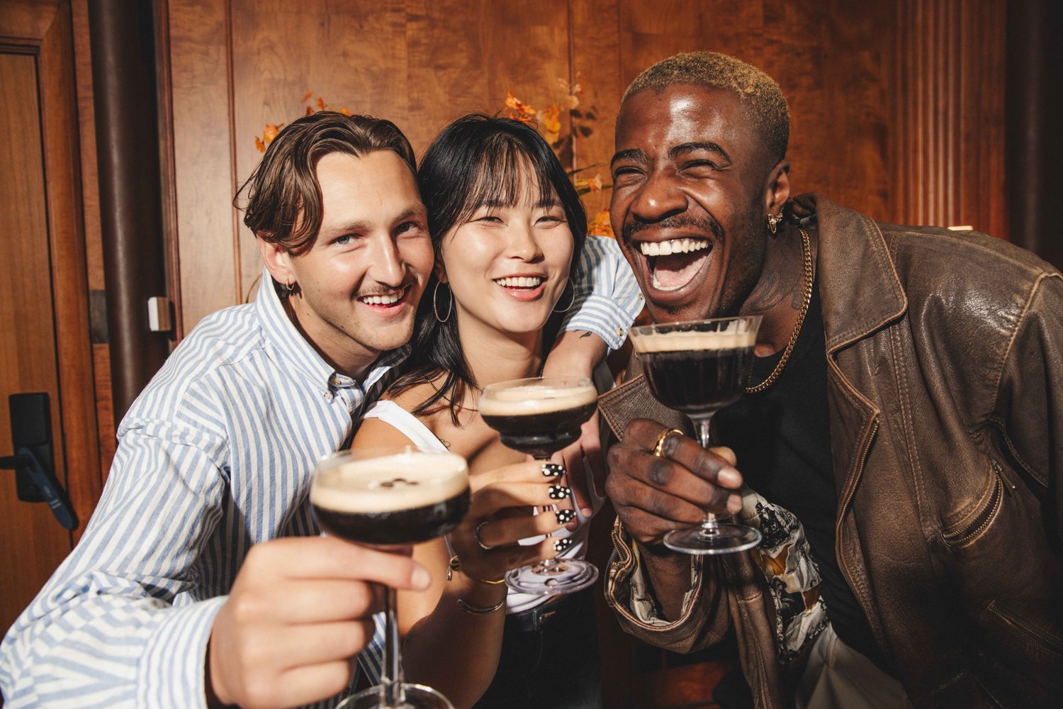 Three friends laughing and raising espresso martinis