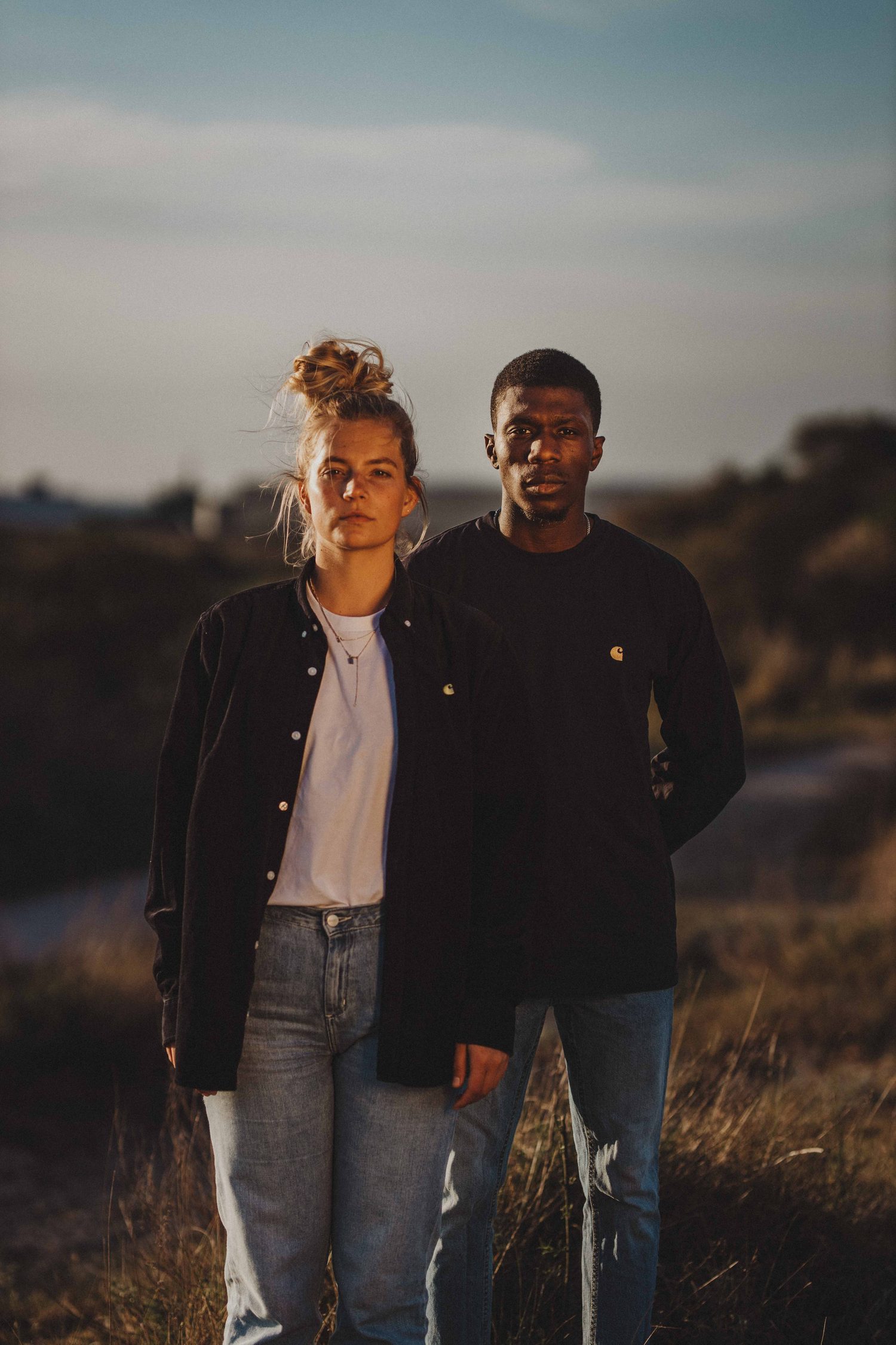 Woman with a hair bun and a man in black standing together in golden light