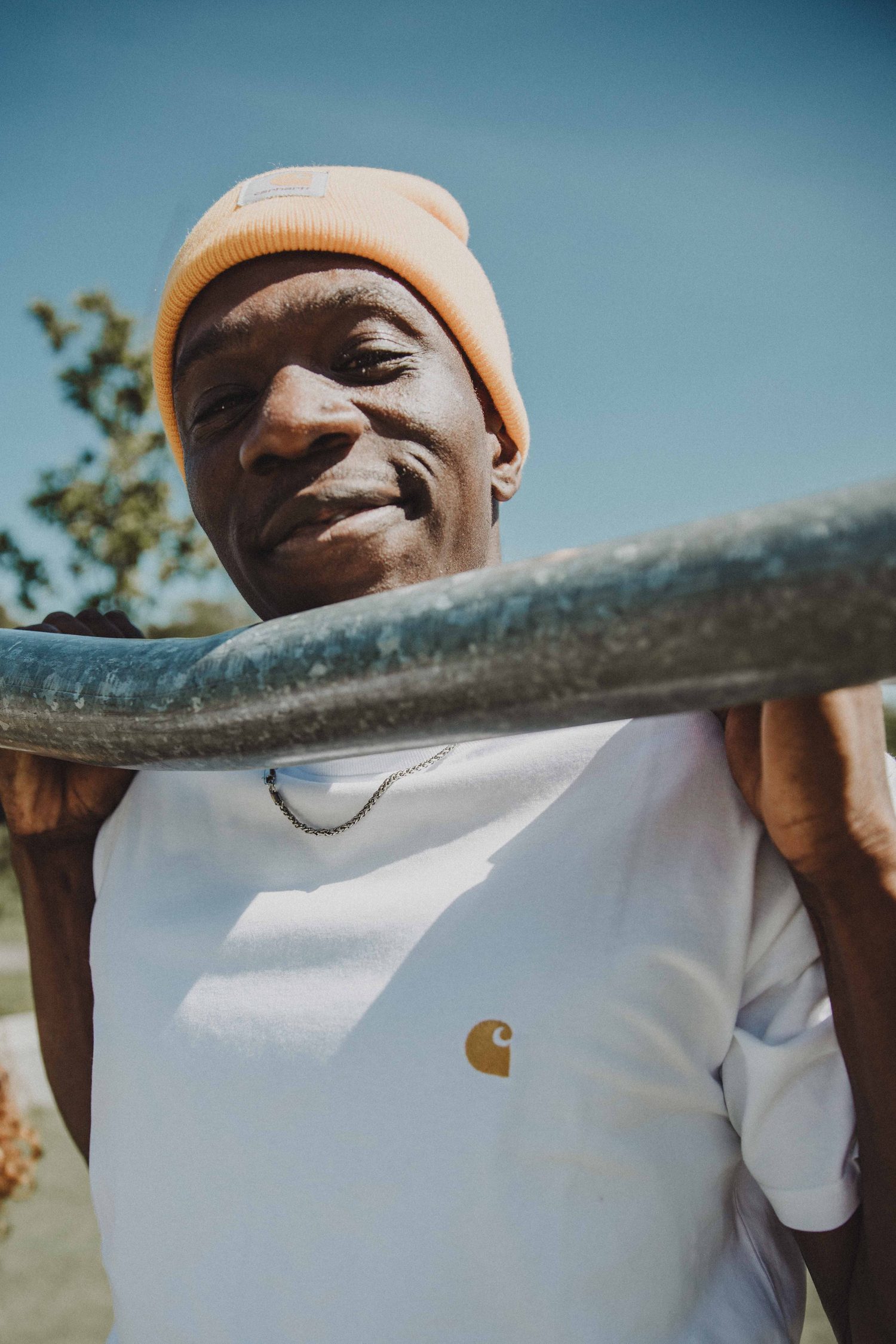 Model in an orange beanie and white Carhartt T-shirt leaning on a metal bar