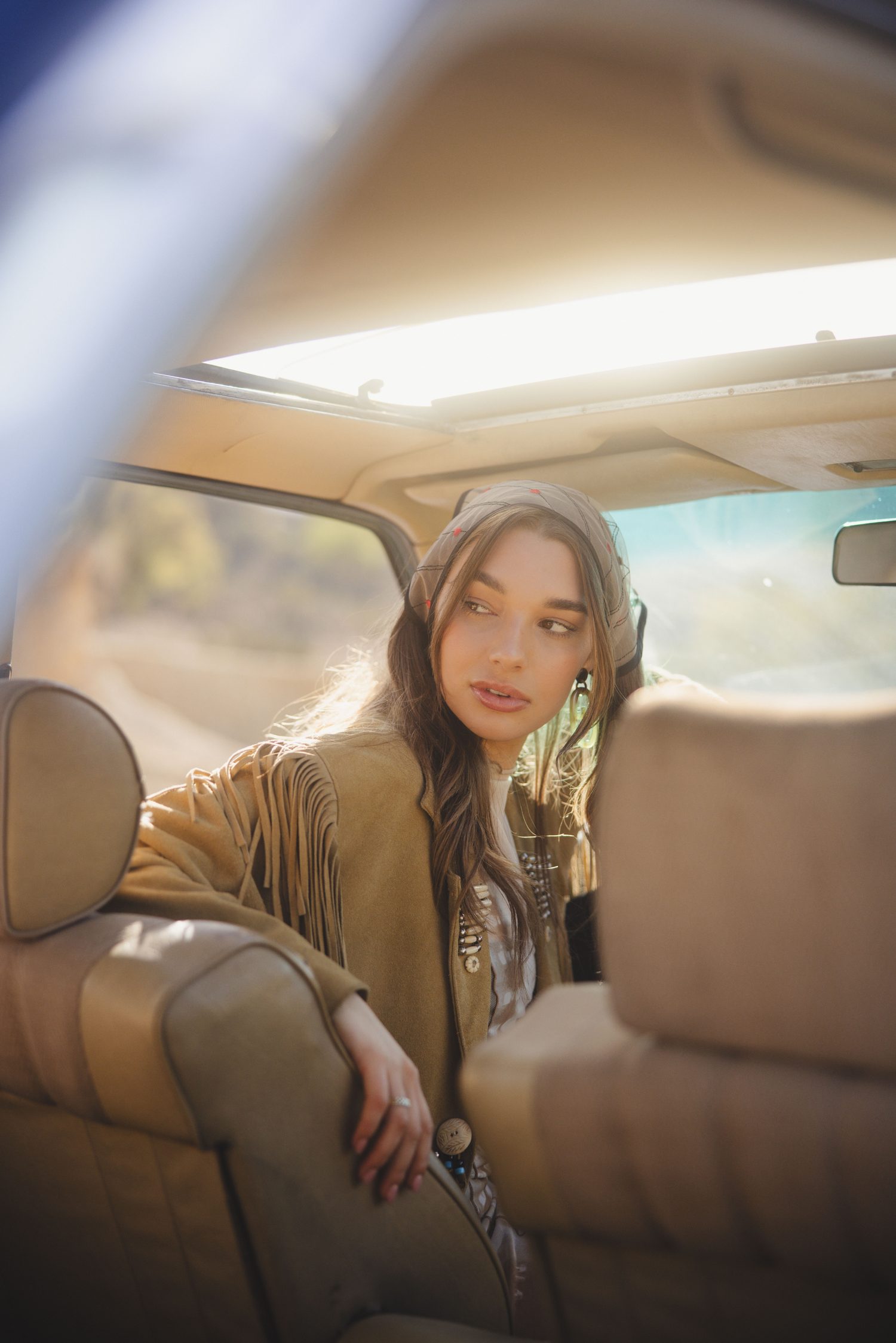 Woman in a headscarf leaning back in the rear seat of a vintage car