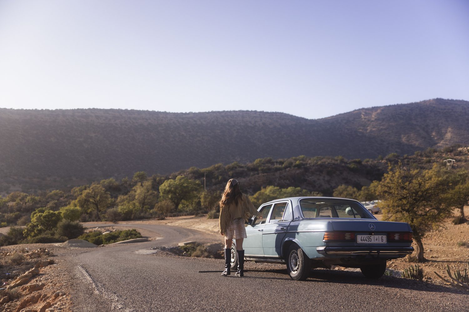 Vintage blue Mercedes parked on an empty mountain road at golden hour