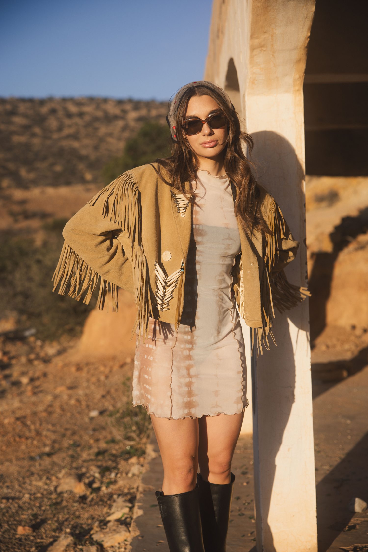 Woman in a fringe jacket by a white concrete arch in the evening sun