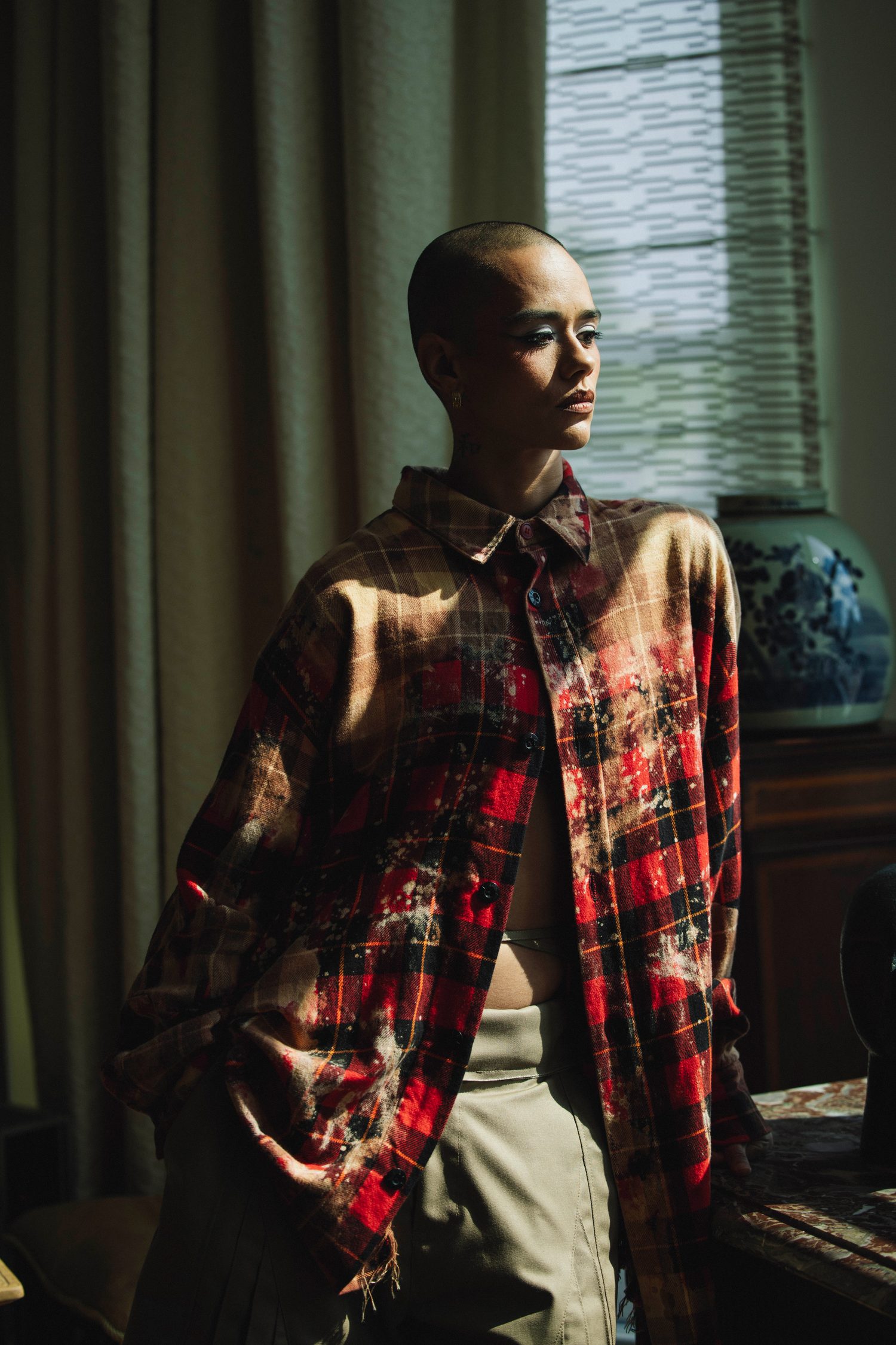 Model in an open plaid shirt standing in window light