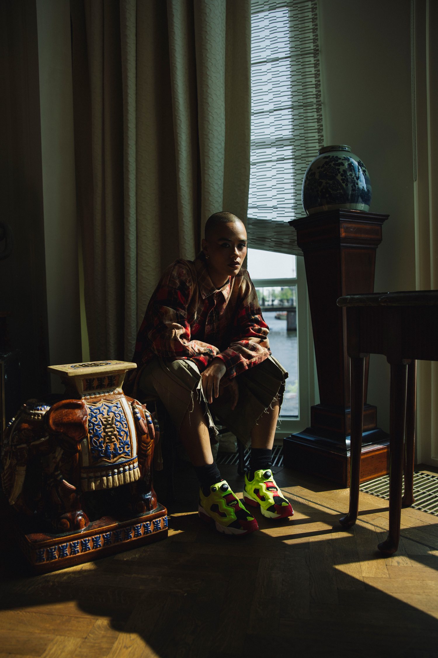Model in a plaid shirt seated on a ceramic elephant stool