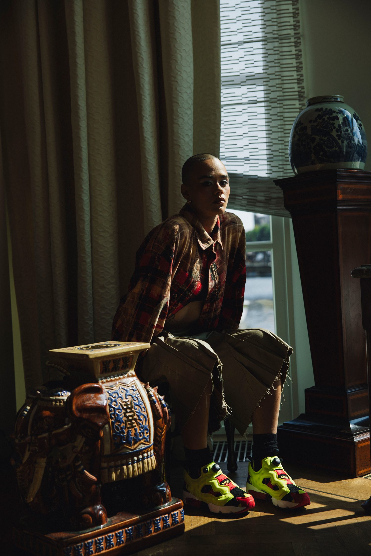 Model in plaid seated by an antique plinth and blue vase