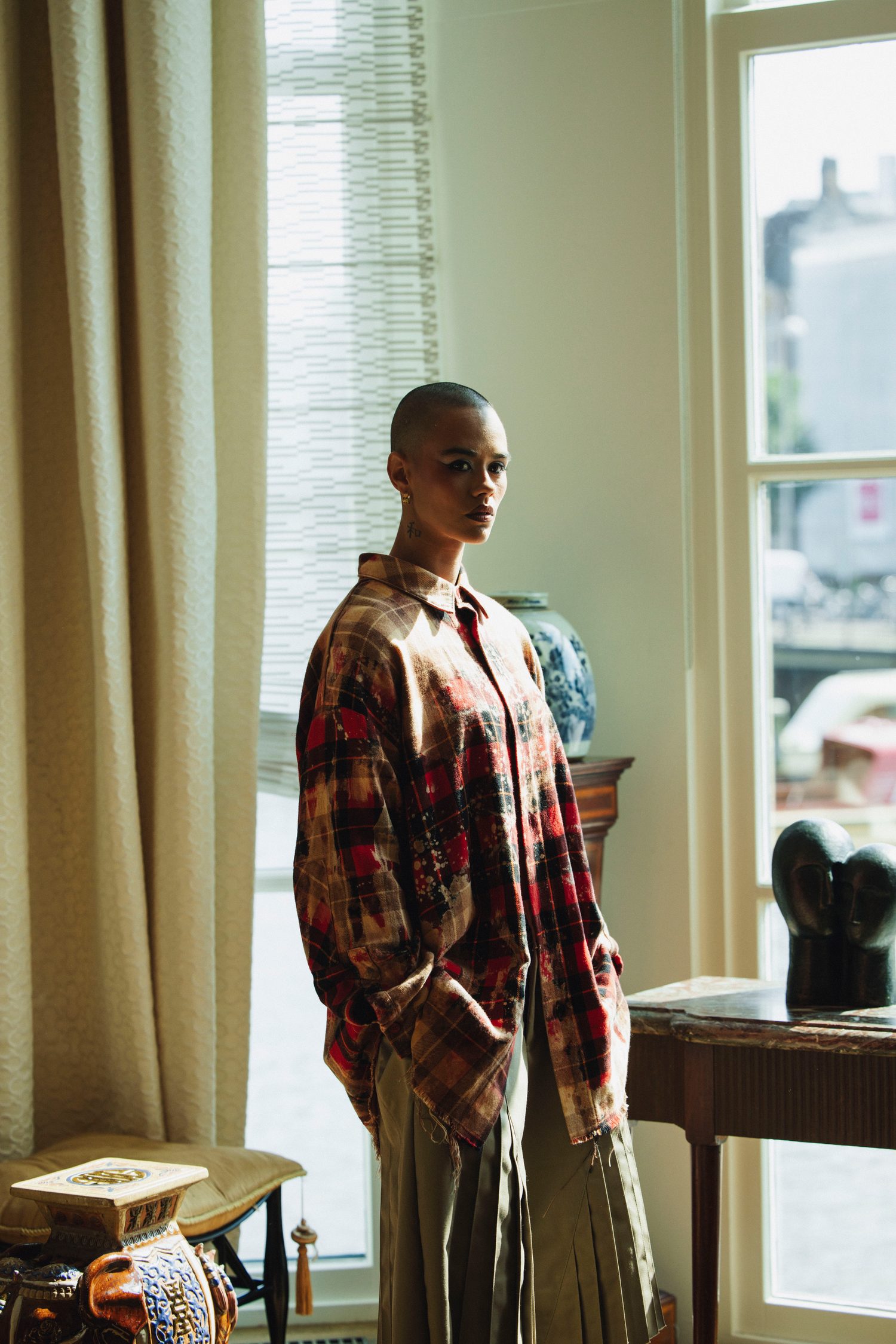 Model in an oversized plaid shirt standing by a tall window