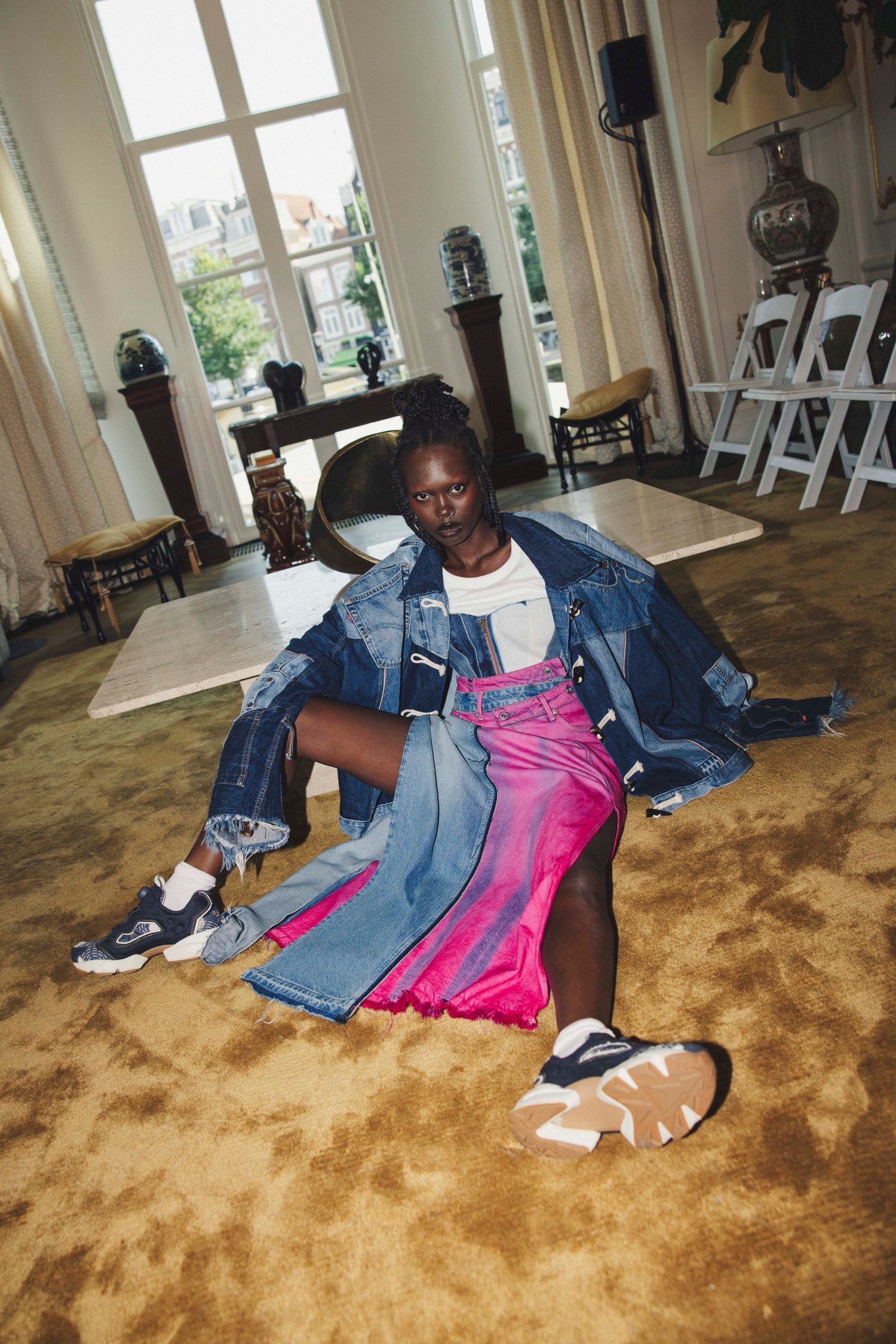 Model in a patchwork denim jacket and pink skirt sprawled on a golden carpet
