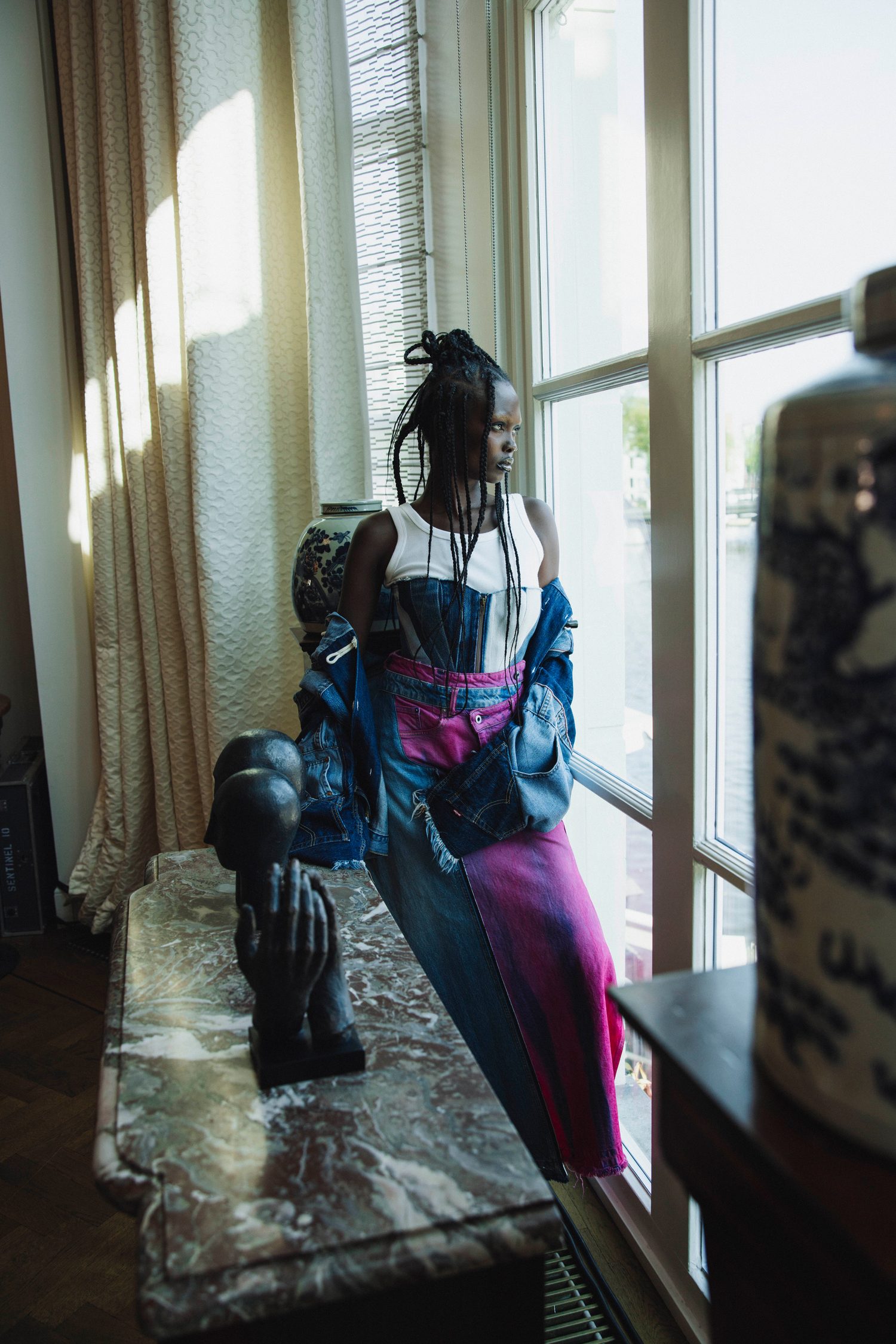 Model with braids standing by a window beside sculpted heads